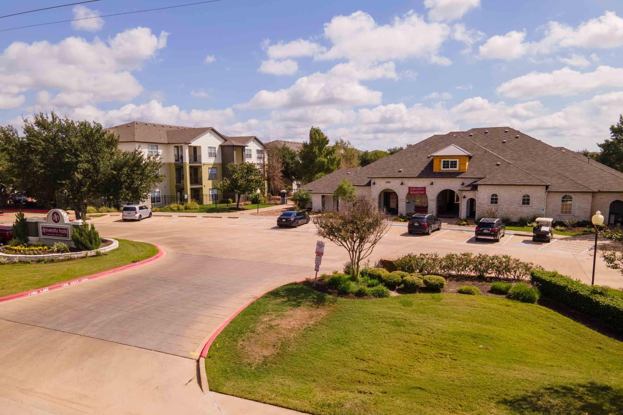 university trails college station off campus apartments near texas a m main entrance driveway and exterior of clubhouse building